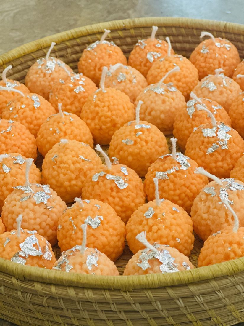 A woven basket full of orange laddoo-shaped candles topped with silver leaf
